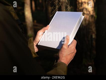 . Männliche Hände, die Buch-Hardcover halten, leeres Hardcover-Cover verspotten in der Natur. Stockfoto