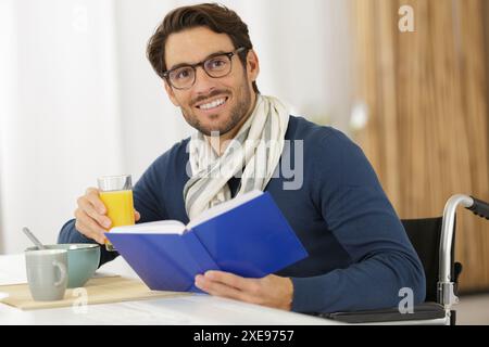 Gutaussehender, fröhlicher, lächelnder Mann im Rollstuhl beim Frühstück Stockfoto