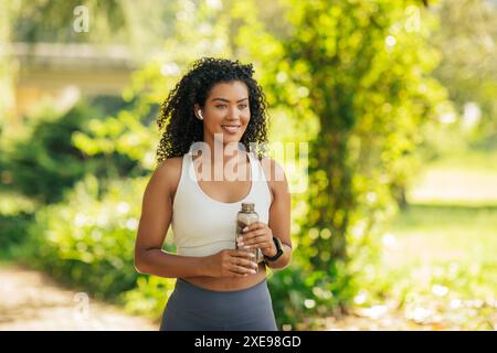 Lächelnde Frau, Die Nach Dem Park-Workout Eine Wasserflasche Hält Stockfoto