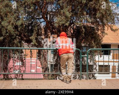Arbeiter in orangefarbener Weste und Sicherheitskleidung ruht auf einem Aussichtspunkt, der sich an Metallzäune lehnt Stockfoto
