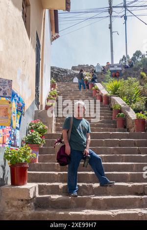 Cusco, Perú; 12. August 2023: Weißer Mann posiert auf mehreren Stufen mit Topfblumen Stockfoto