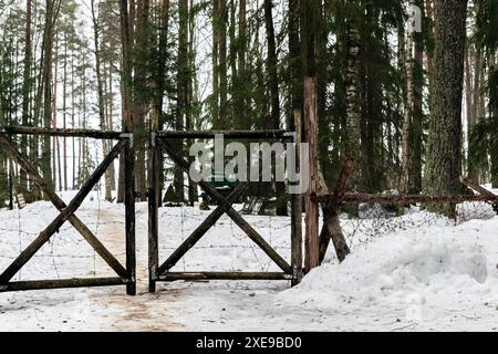 Altes hölzernes Tor, verwickelt mit eisernem Stacheldraht. Vor dem Hintergrund eines Winterwaldes. Stockfoto