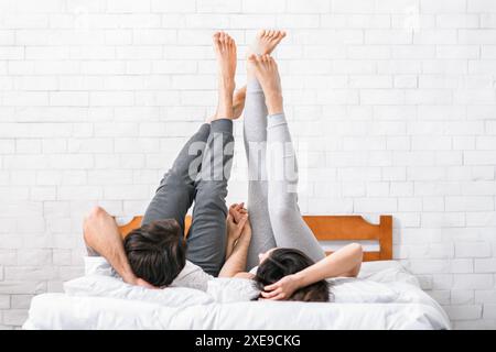 Ein Paar hält die Hände, während er mit erhobenen Beinen auf dem Bett liegt Stockfoto