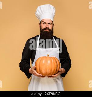 Seriöser männlicher Koch in Uniform mit Kürbis. Herbstrezepte. Koch in weißer Schürze mit Kürbis zum Kochen. Thanksgiving-Tag. Bärtiger Mann in Stockfoto