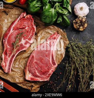 Zwei rohe Rindersteaks auf einem hölzernen Schneidebrett, Knoblauch und ein Zweig Rosmarin Stockfoto