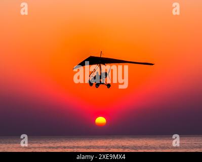 Motorisierter Segelflugzeug fliegt gegen den Sonnenuntergang über dem Meer. Stockfoto