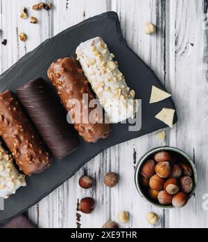 Französische Dessert-Eclairs oder Profiterolen mit verschiedenen Schokoladenglasur auf einem schwarzen Steinteller Stockfoto