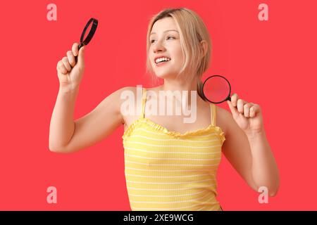 Junge Frau mit Lupen auf rotem Hintergrund Stockfoto