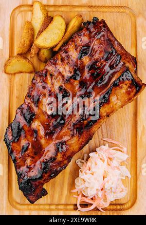 Schweinerippchen, serviert auf Schneidebrett und Kartoffelscheiben Stockfoto