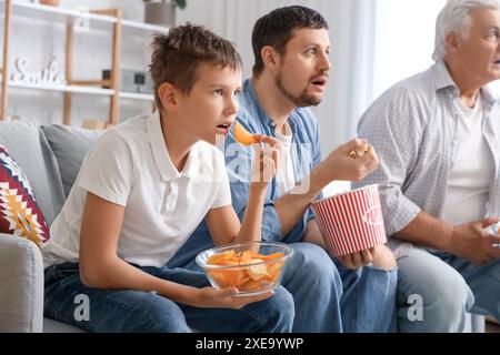 Überraschte Familie beim Essen, während sie zuhause Fußballspiele auf dem Sofa ansah Stockfoto
