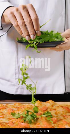 Der Koch dekoriert Lachspizza mit Rucola Stockfoto