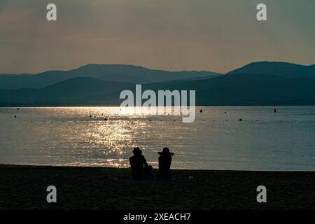 Romantisches Paar, das bei Sonnenuntergang am Strand sitzt Stockfoto