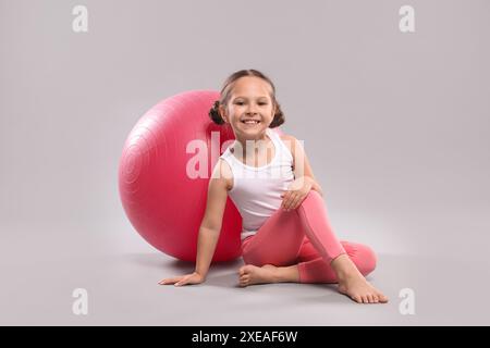 Niedliches kleines Mädchen mit passendem Ball auf grauem Hintergrund Stockfoto