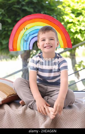 Ein glücklicher kleiner Junge in der Nähe von Regenbogenmalerei am Fenster drinnen Stockfoto