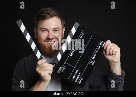 Filme machen. Lächelnder Mann mit Klapptafel auf schwarzem Hintergrund Stockfoto