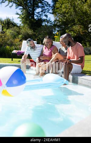 Verschiedene Seniorenfreunde sitzen am Pool und genießen den sonnigen Tag zusammen Stockfoto