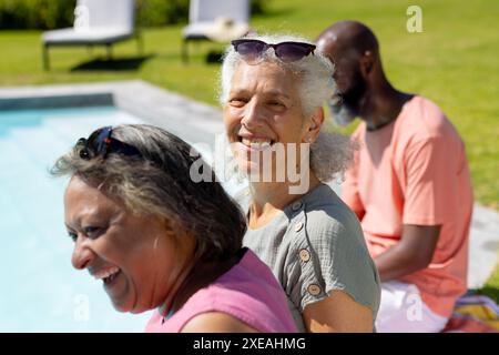 Am Pool lächelnd und entspannend, verschiedene Seniorenfreunde genießen den sonnigen Tag Stockfoto