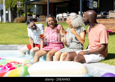 Verschiedene Seniorenfreunde sitzen am Pool, genießen Getränke und lachen Stockfoto