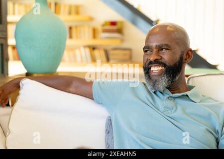 Lächelnder afroamerikanischer Mann, der sich zu Hause auf der Couch entspannt und die Freizeit genießt Stockfoto