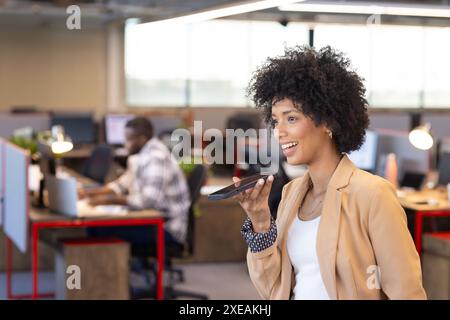 Mit Smartphone für Sprachnachrichten, Geschäftsfrau lächelt im modernen Büro Stockfoto