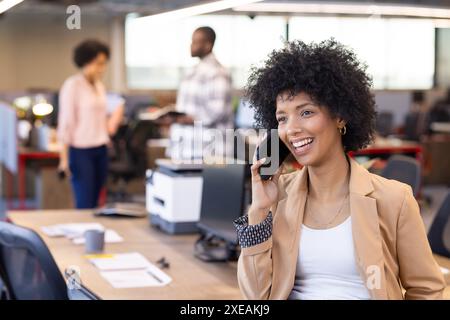 Sie spricht auf dem Smartphone, eine afroamerikanische Geschäftsfrau lächelt im modernen Büro Stockfoto