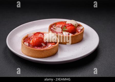 Köstliche frische süße Törtchen mit Erdbeeren und Kokosflocken auf dunklem Betonhintergrund Stockfoto