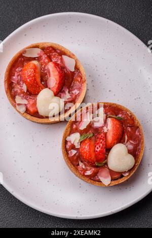 Köstliche frische süße Törtchen mit Erdbeeren und Kokosflocken auf dunklem Betonhintergrund Stockfoto