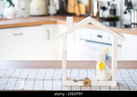 Schlüssel und winziges Haus mit gemütlichem Haus mit Osterdekor mit Kaninchen und Eiern auf dem Tisch der Küche. Gebäude, Design, Projekt, Umzug nach Stockfoto