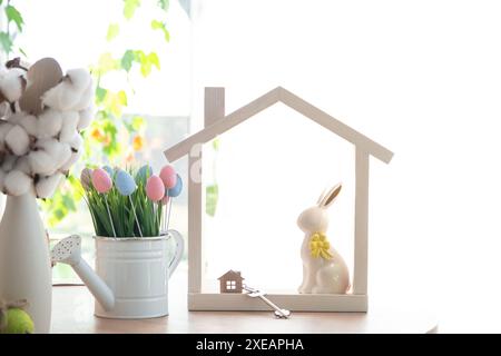 Schlüssel und winziges Haus mit gemütlichem Haus mit Osterdekor mit Kaninchen und Eiern auf dem Tisch der Küche. Gebäude, Design, Projekt, Umzug nach Stockfoto