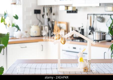 Schlüssel und winziges Haus mit gemütlichem Haus mit Osterdekor mit Kaninchen und Eiern auf dem Tisch der Küche. Gebäude, Design, Projekt, Umzug nach Stockfoto