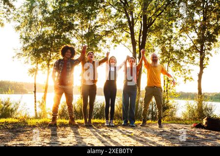 Jubilant Lakeside Victory: Freunde feiern im Sonnenuntergang Stockfoto