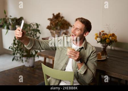 Porträt eines hübschen, glücklichen jungen Mannes, Selfie im Café, posieren mit einer Tasse Kaffee, Video-Chats mit Smartphone-App, Gespräche Stockfoto