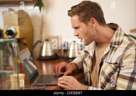 Das Porträt eines Mannes sieht frustriert auf dem Laptop-Bildschirm aus, starrt mit schockiertem Gesichtsausdruck auf den Monitor, liest eine Nachricht mit runzeligen Gesichtern Stockfoto
