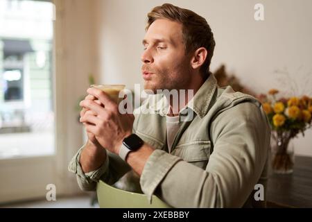 Porträt eines jungen gutaussehenden bärtigen Mannes im Café, der auf einem Stuhl sitzt, Cappuccino schlürft, im Café ausruht Stockfoto