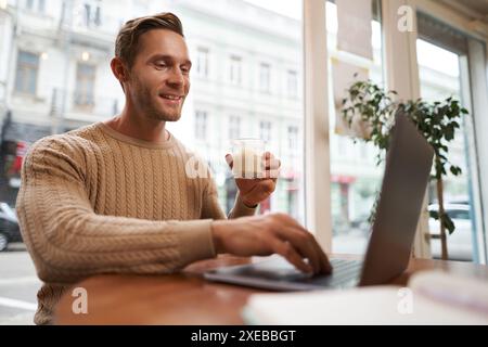 Porträt eines jungen Geschäftsmannes im Café, der Kaffee trinkt und seinen Laptop benutzt, vom Coworking Space aus arbeitet, in der Nähe des Cafés sitzt Stockfoto