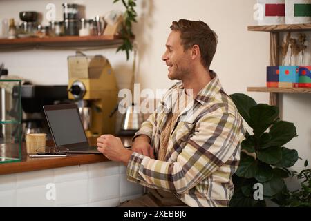 Porträt eines gutaussehenden Geschäftsmannes, jungen digitalen Nomaden, der im Café sitzt und auf seinen Laptop-Bildschirm blickt, aus der Ferne arbeitet, tut Stockfoto