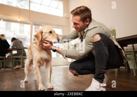 Nahaufnahme Porträt eines hübschen glücklichen Mannes, der seinen süßen Hund in einem haustierfreundlichen Café streichelt. Coffee-Shop-Besucher mit seinem goldenen Retriev Stockfoto