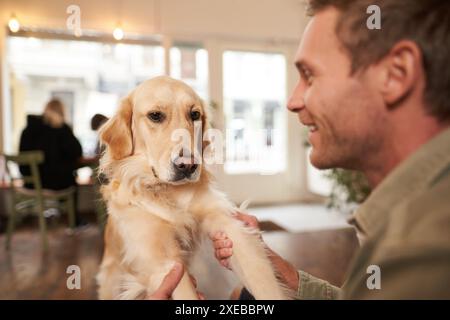 Nahporträt eines jungen Mannes mit seinem Haustier im Café. Hundebesitzer spielt mit seinem Haustier und sieht glücklich aus Stockfoto