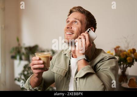 Porträt eines hübschen jungen Mannes, der am Telefon spricht, im Café sitzt und Kaffee trinkt, einen Anruf entgegennimmt Stockfoto