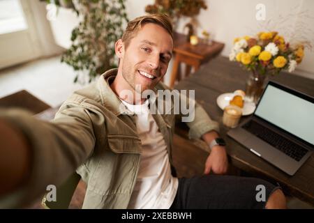 Selfie-Porträt eines hübschen jungen Mannes, der sich im Café mit Laptop fotografiert und in die Kamera lächelt Stockfoto