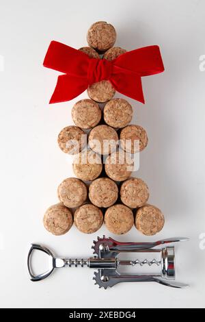 Sektkorken und ein Korkenzieher aus Metall sind in Form eines Weihnachtsbaums mit einer roten Satinschleife auf weißem Hintergrund angelegt Stockfoto