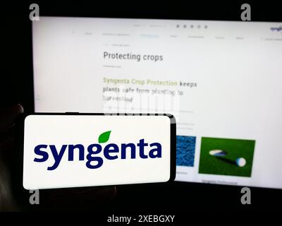 Person mit Mobiltelefon mit Logo der Schweizer agritech-Gesellschaft Syngenta Crop Protection AG vor der Business-Webseite. Schwerpunkt auf dem Display des Telefons. Stockfoto