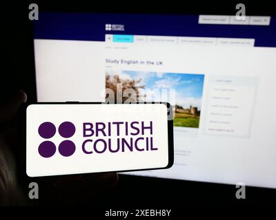 Person mit Smartphone und Logo der Kultur- und Bildungsorganisation British Council vor der Website. Schwerpunkt auf dem Display des Telefons. Stockfoto