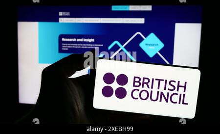 Person, die ein Mobiltelefon mit dem Logo der Kultur- und Bildungsorganisation British Council vor der Webseite hält. Schwerpunkt auf dem Display des Telefons. Stockfoto