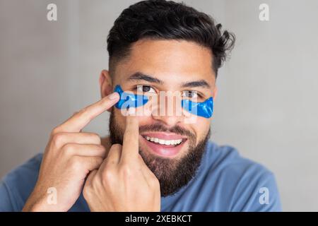 Blaue Flecken unter den Augen auftragen, ein Mann lächelt und zu Hause auf sie zeigt Stockfoto