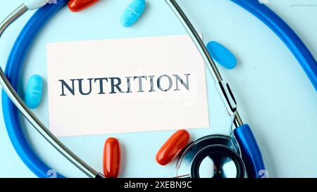 NÄHRWERTWORT auf einer weißen Visitenkarte auf blauem Hintergrund mit einem Stethoskop, Pillen in einer Komposition in kalten Tönen Stockfoto