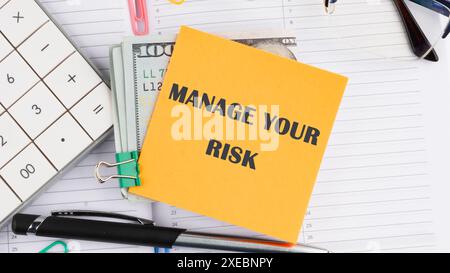 Geschäftskonzept. Schreiben Sie IHR RISIKO auf einem gelben Aufkleber neben amerikanischen 100-Dollar-Scheinen, einem Taschenrechner, einem Stift auf weißem Hintergrund Stockfoto
