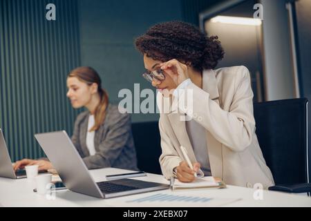 Fokussierte junge Geschäftsfrauen verwenden Gadgets, während sie im Coworking arbeiten. Konzept der Fernarbeit Stockfoto