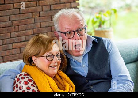 Fröhliches Seniorenpaar mit überraschendem Ausdruck in gemütlichem Zuhause Stockfoto