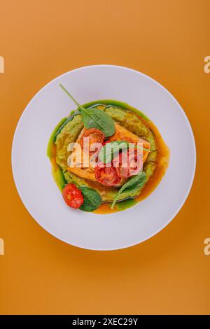 Lachssteak mit Avocadopüree, dekoriert mit Basilikumblättern und Kirschtomaten Stockfoto